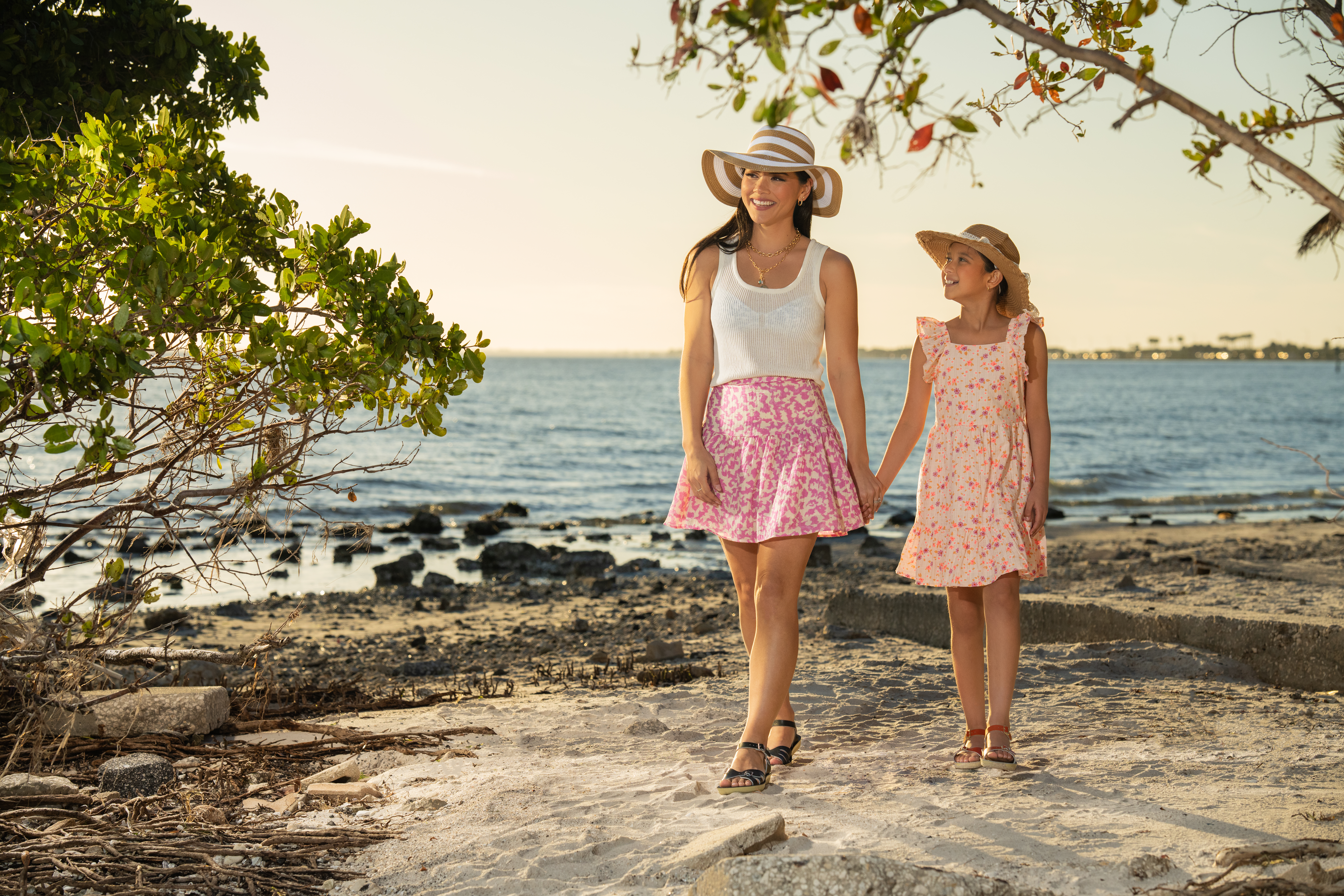 A woman and a child walking hand-in-hand on a beach modeling for Drive Social Media's ecommerce photoshoot.