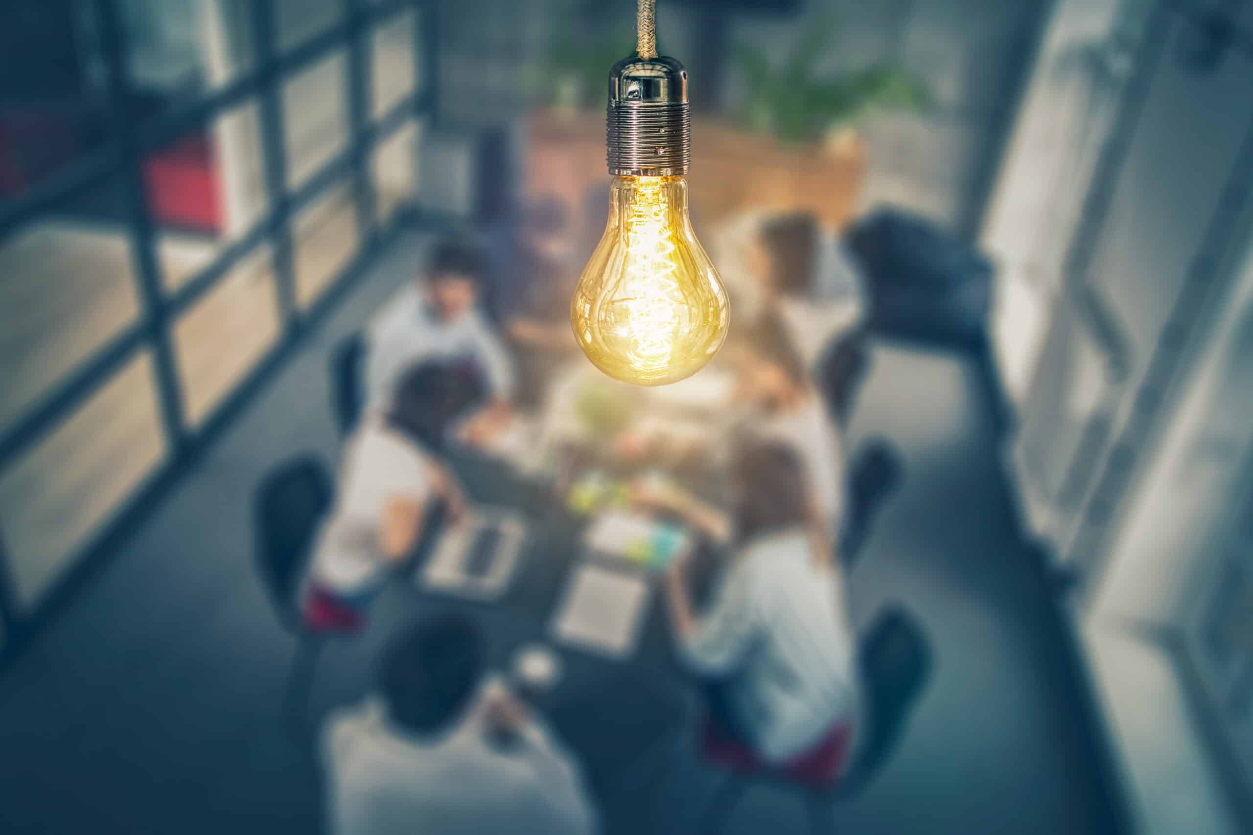 Light bulb symbolizing innovation with a blurred background of a team meeting, representing continuous learning and collaboration in social media marketing.