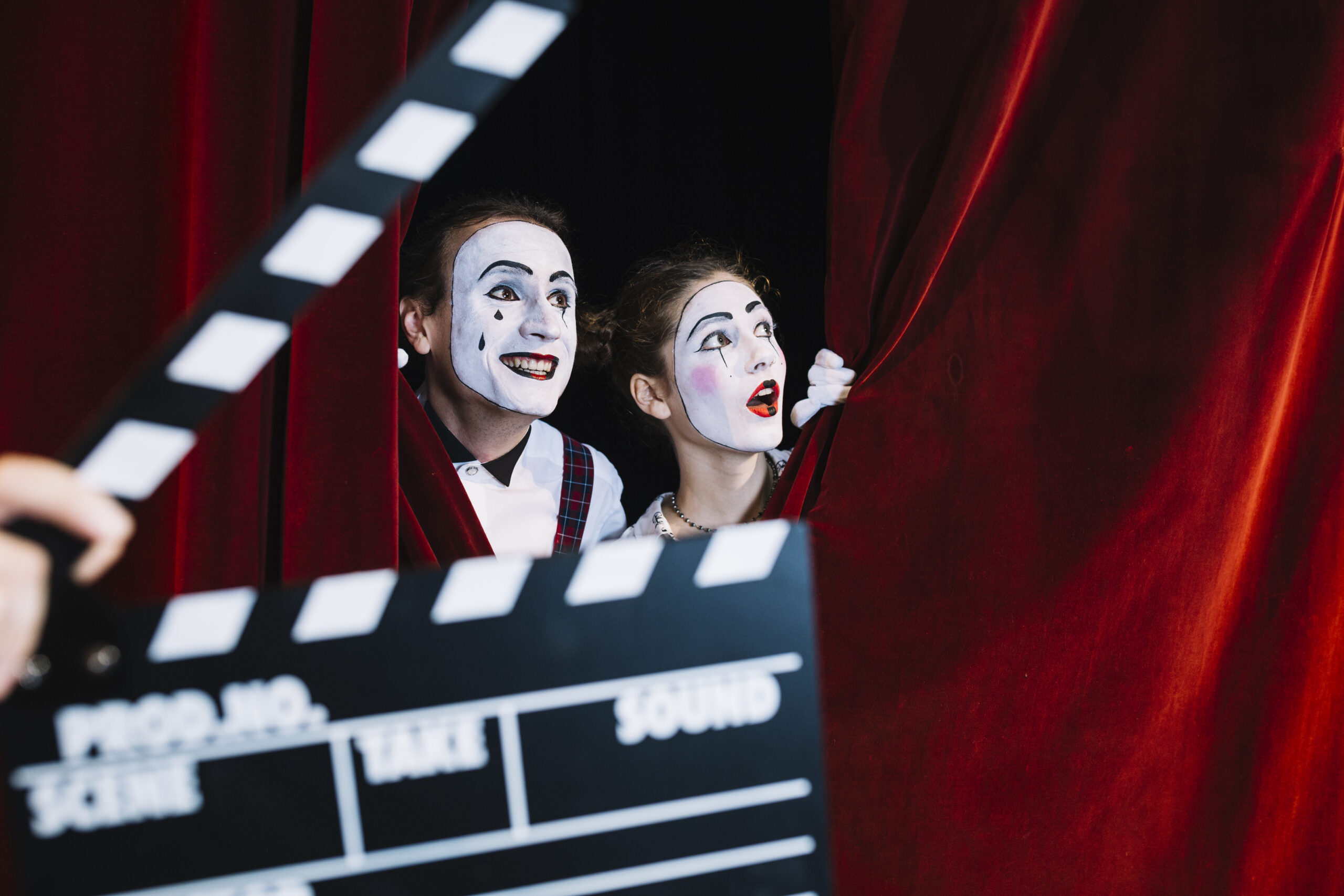 Mime actors peeking through red theater curtains with a clapperboard, representing performance and storytelling in digital marketing