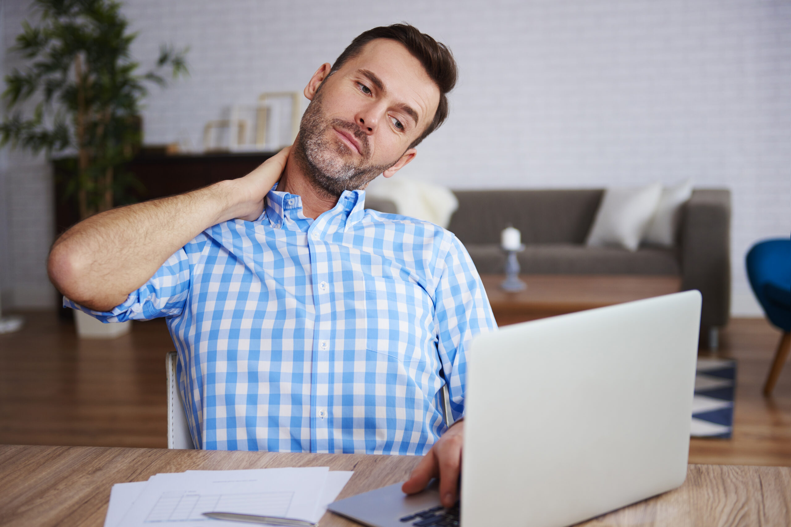 Man at his laptop rubbing a tense, knotted neck while working, illustrating the unaddressed tension that quietly builds in relationships.